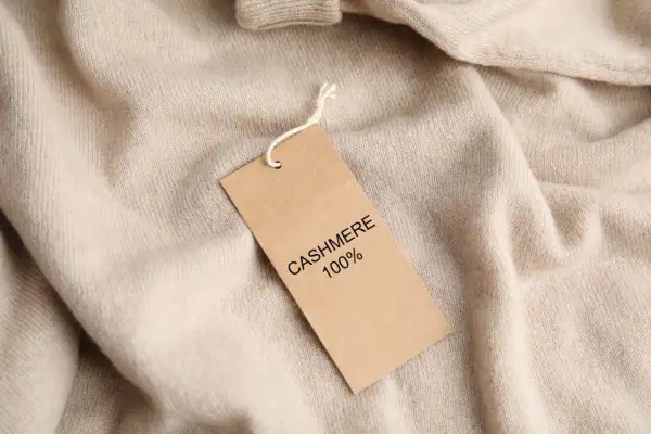 Ein Etikett auf einem beigefarbenen Pullover erklärt, woraus Kaschmir besteht: 100% Kaschmir.
